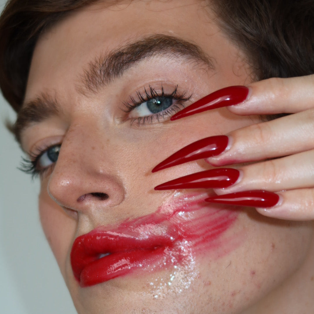 Close-up of a person with red lipstick and nails, covering part of their face.